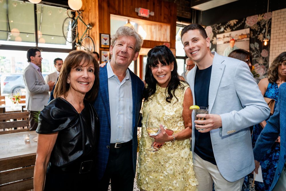 Four adults smiling and posing together at a casual indoor social gathering or party event.