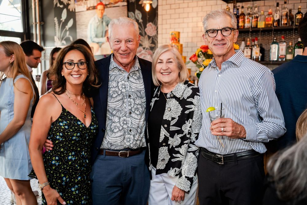 Four smiling adults posing together at an upscale restaurant bar during a social gathering event.