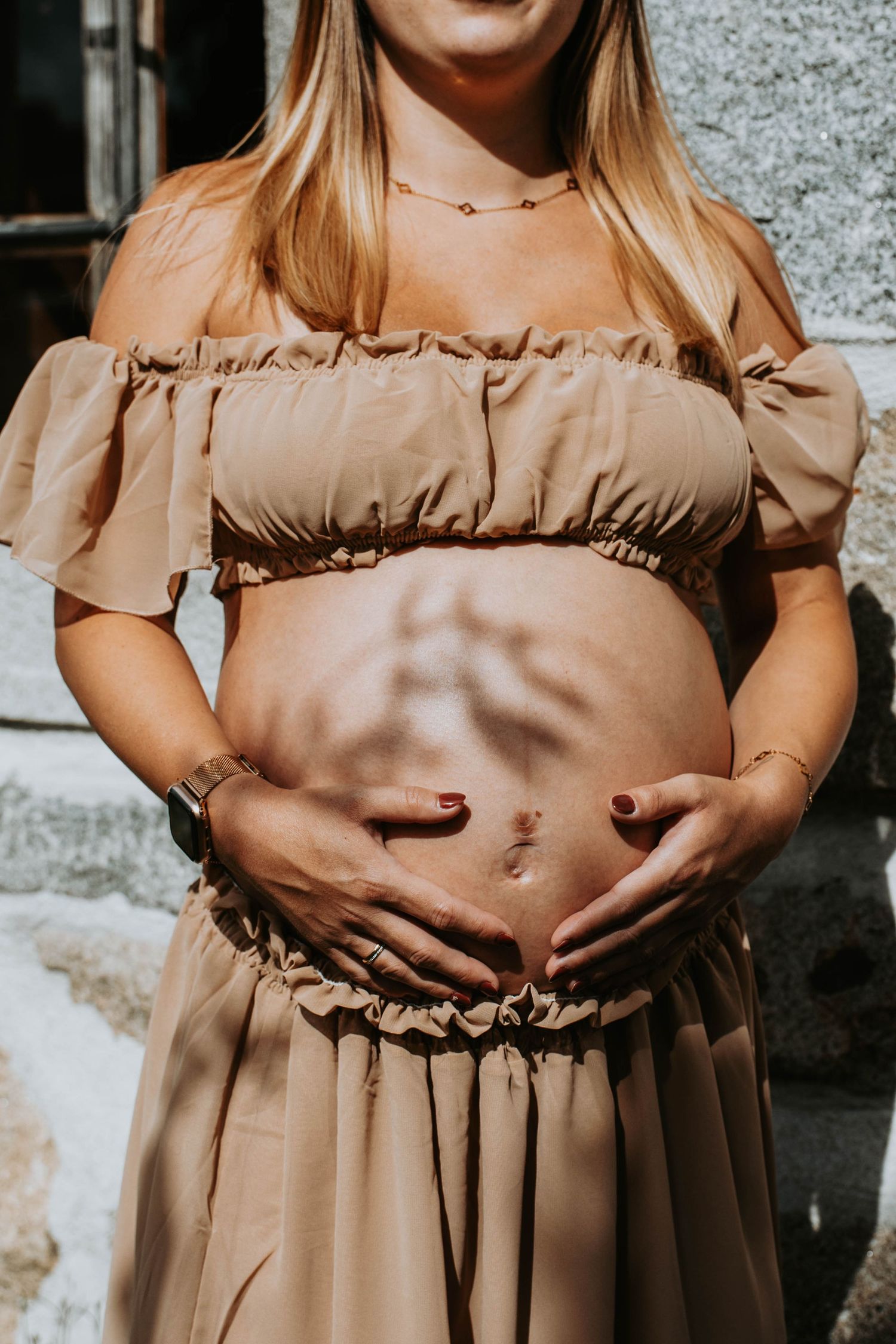 Sepia-toned maternity photo of a pregnant belly with hands cradling it, wearing a ring, by Rene Resch Fotografie.