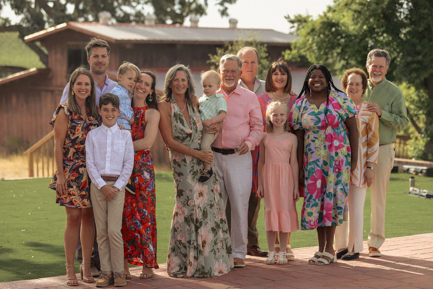 Large multigenerational family posing together outdoors on a sunny day, smiling for a formal group portrait.