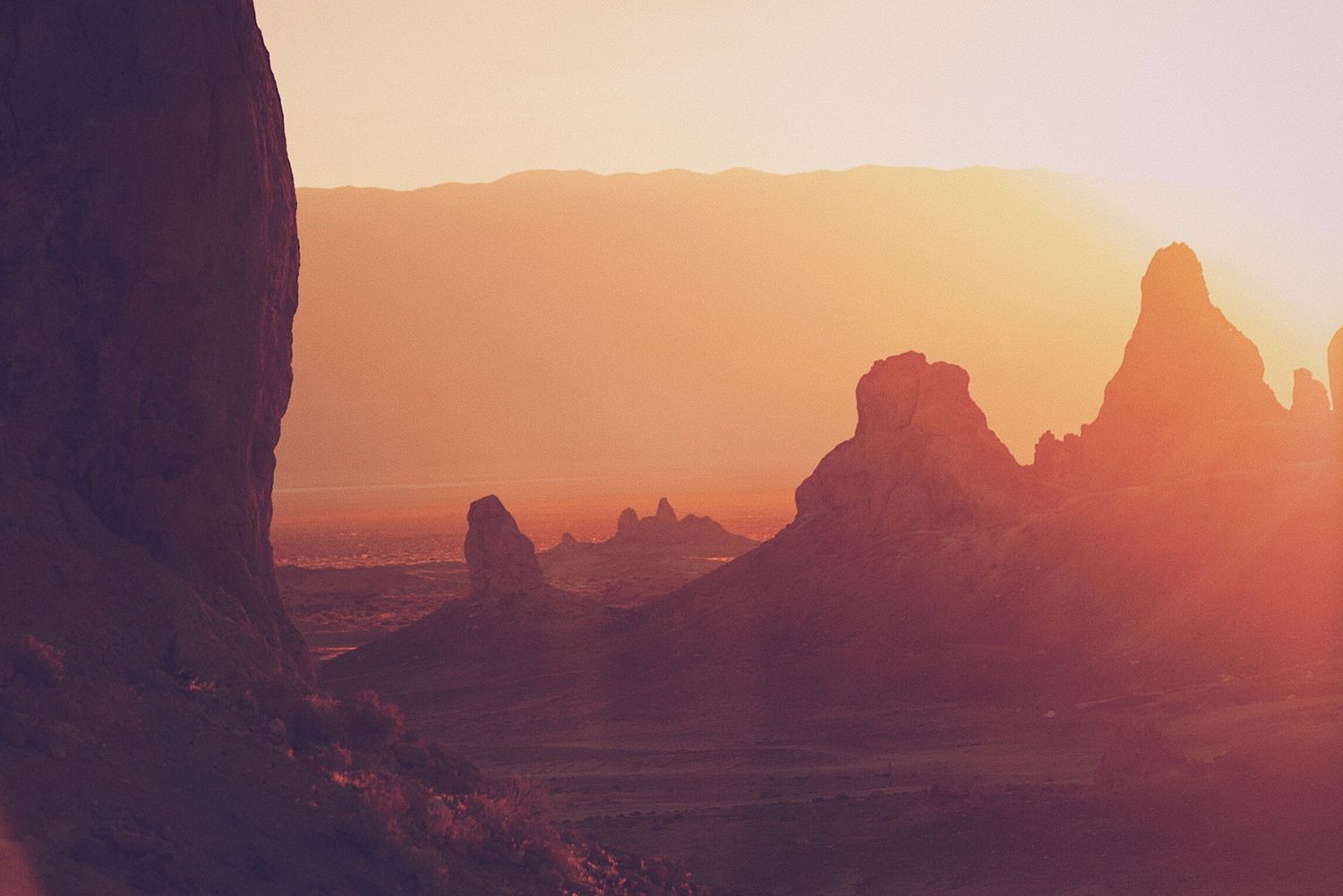 Dramatic rock formations silhouetted against an orange desert sunset.