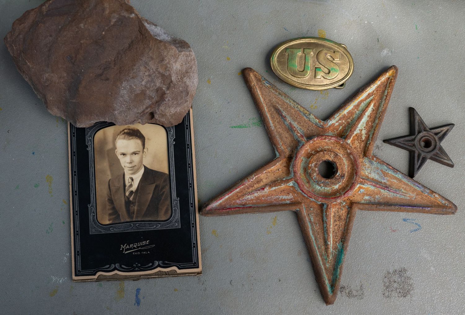 Antique collection featuring a vintage portrait photo, rusty metal star, US military belt buckle, and a rock on a gray surface.