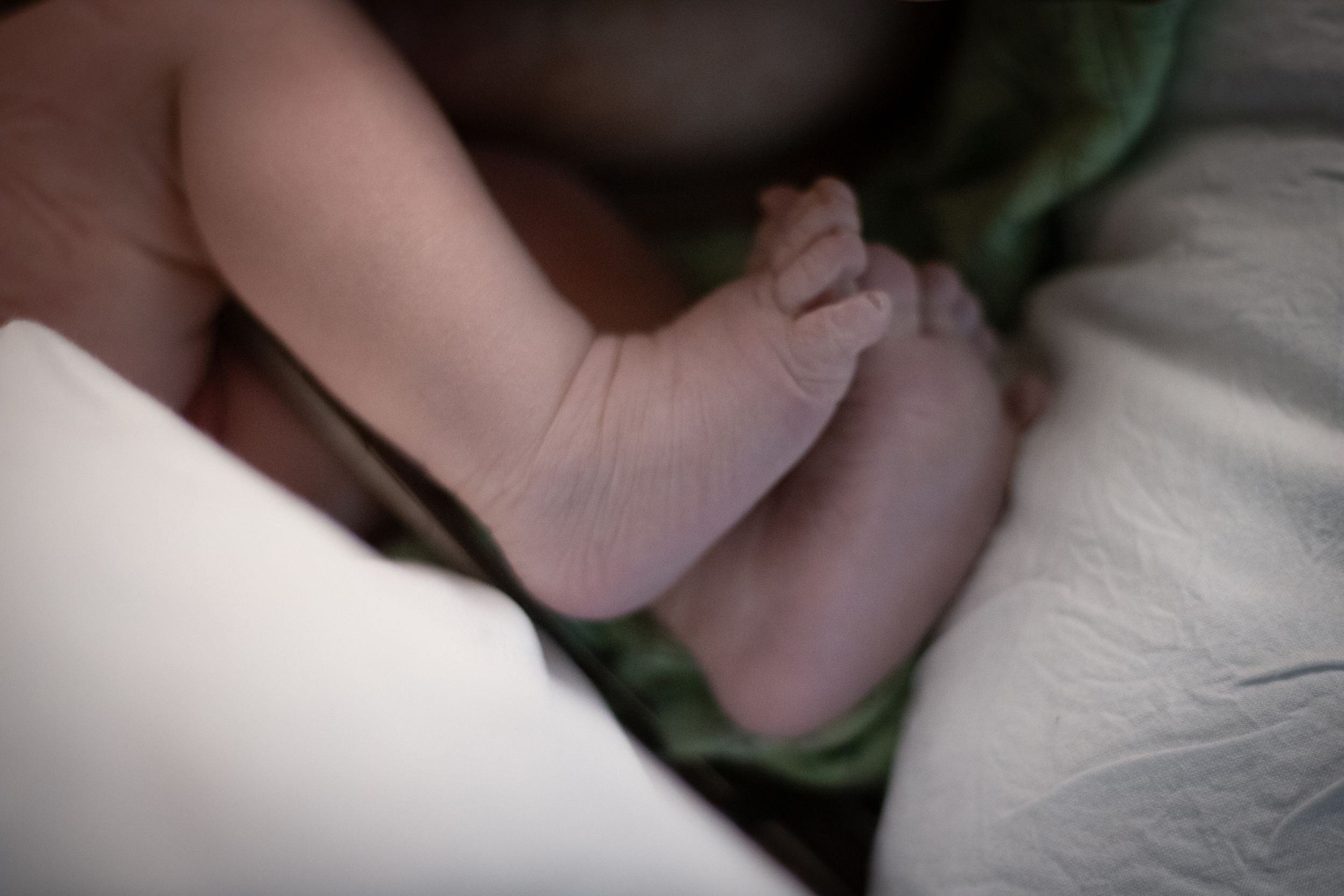 Delicate newborn baby feet resting on soft white and green blankets.