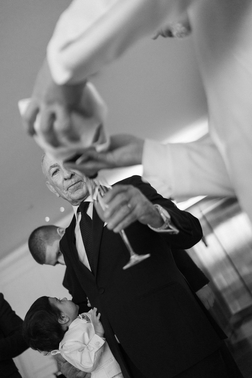 Black and white photo of an elderly man in a suit raising a champagne glass during a wedding toast.