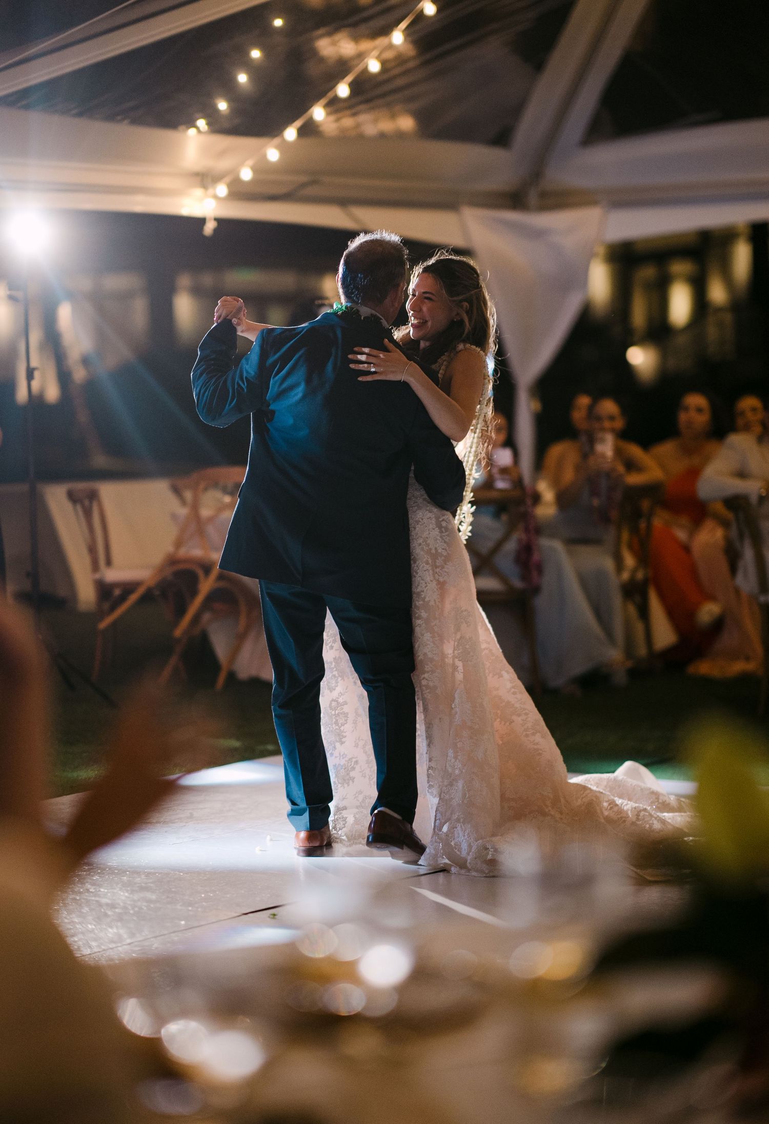 Bride and groom share their first dance under string lights at an elegant outdoor wedding reception.