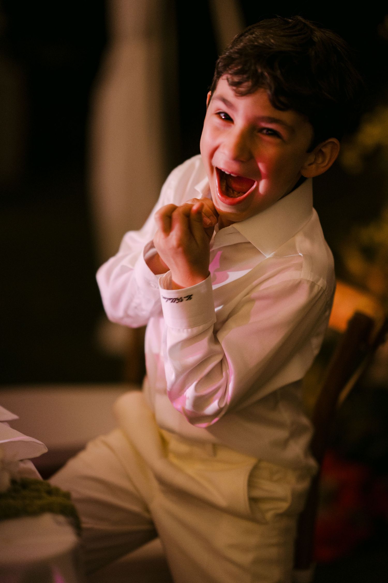 Joyful young boy in white dress shirt laughing at a formal event, captured in warm evening light.