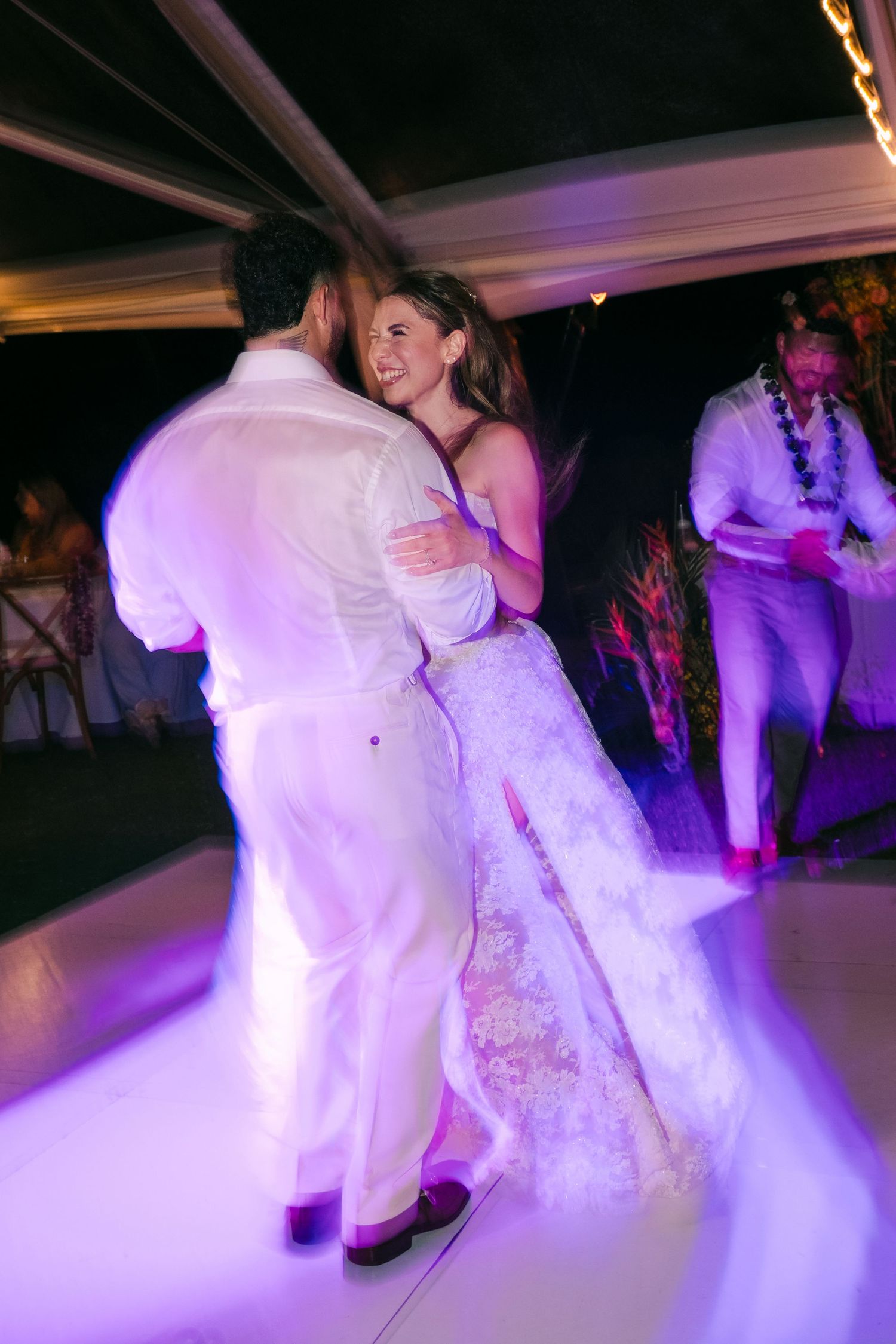 Bride and groom share their first dance on a glowing purple dance floor at an elegant wedding reception.