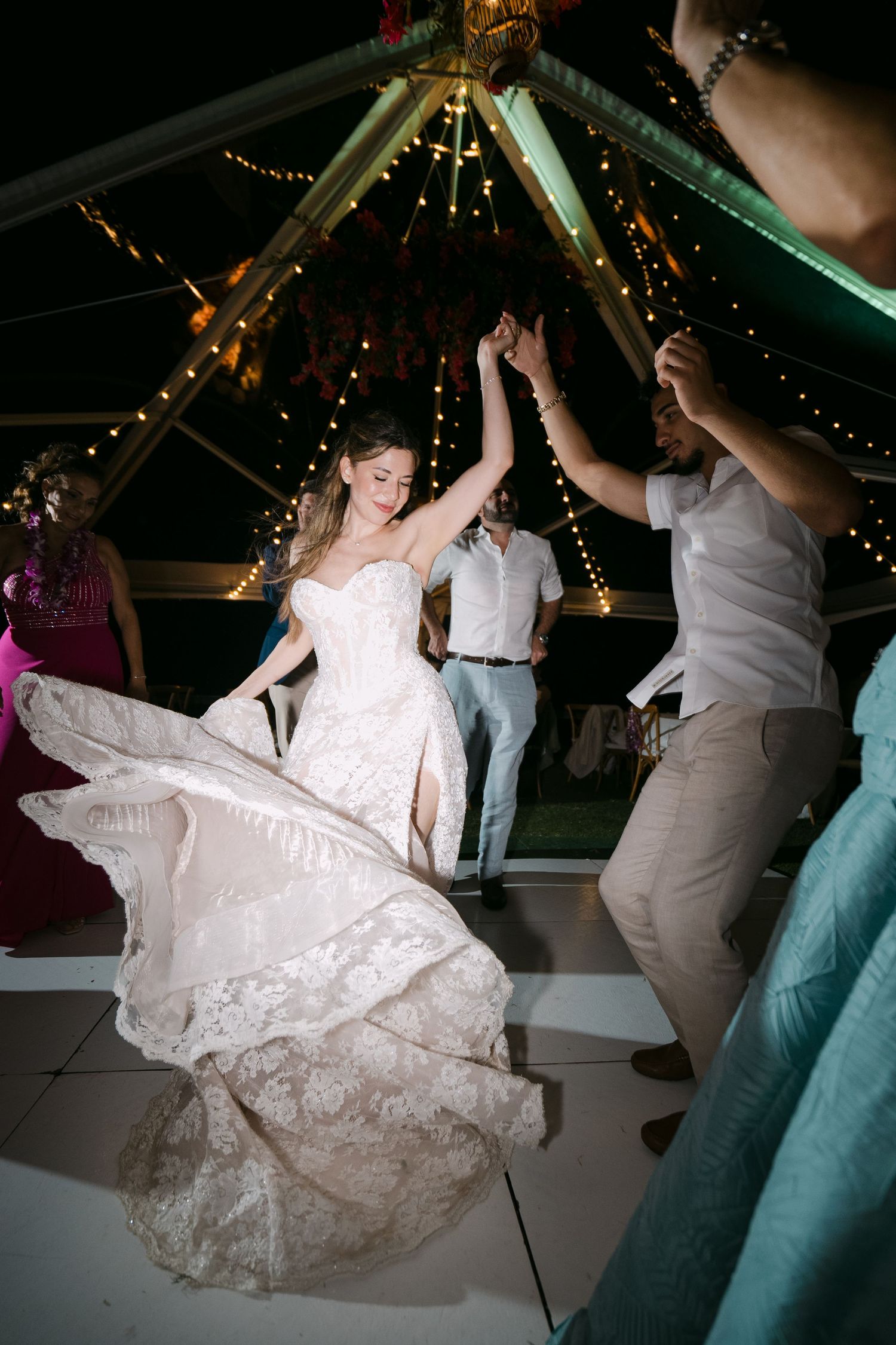 Bride twirling in lace wedding dress on dance floor under fairy lights at elegant outdoor wedding reception.