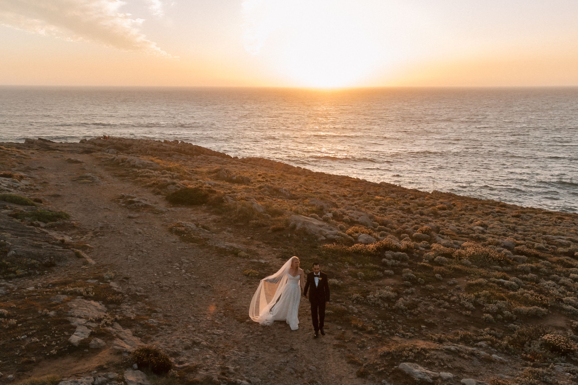 Aerial wedding portrait of the bride and groom at sunset on the dramatic cliffs of Cascais.
