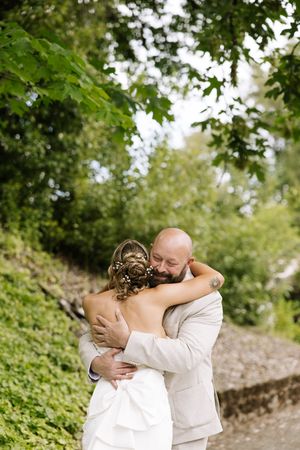Bride and groom share a tender embrace outdoors, surrounded by lush green trees on their wedding day.