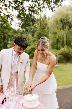 Smiling bride and groom cutting their white wedding cake outdoors at a garden reception.