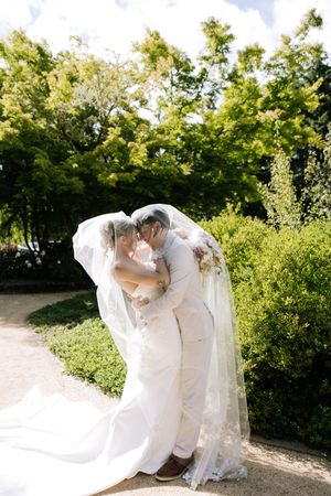 Bride and groom sharing a romantic kiss under a flowing veil in a lush garden on their wedding day.