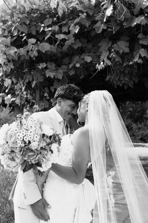 Black and white photo of bride and groom sharing a tender kiss under garden vines.