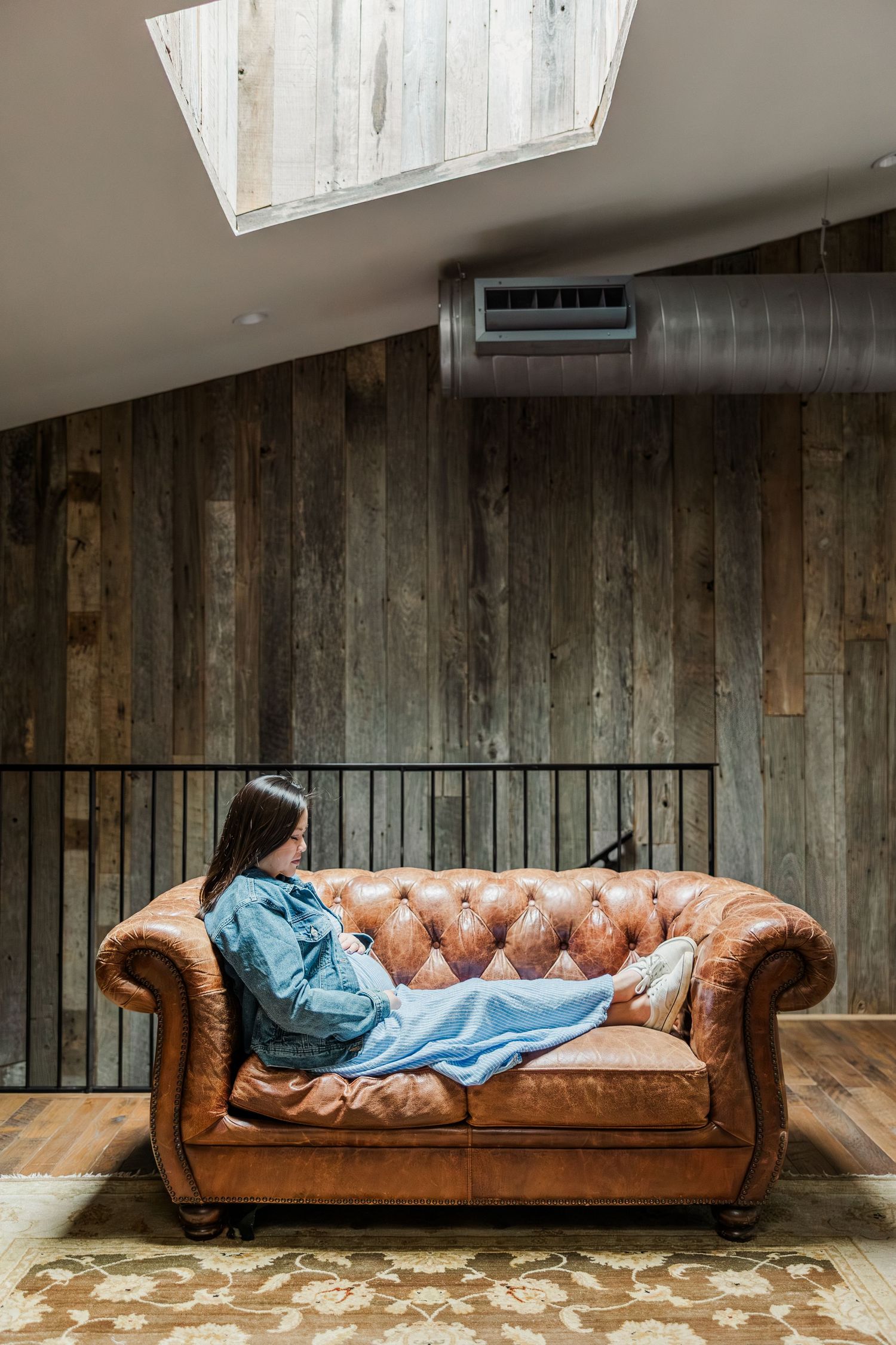 Young woman relaxing on a tufted leather Chesterfield sofa with a blue blanket in a rustic loft space.