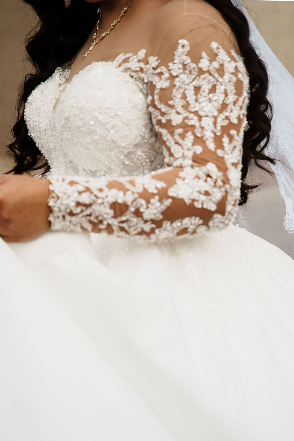 Close-up of a bride wearing an elegant lace wedding gown with sheer long sleeves and intricate floral beading.