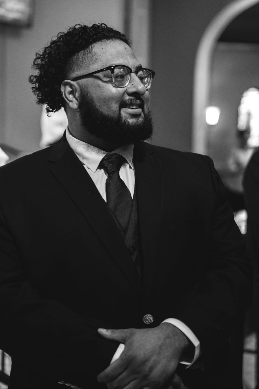 Black and white portrait of a bearded man wearing glasses and a suit with tie at a formal event.