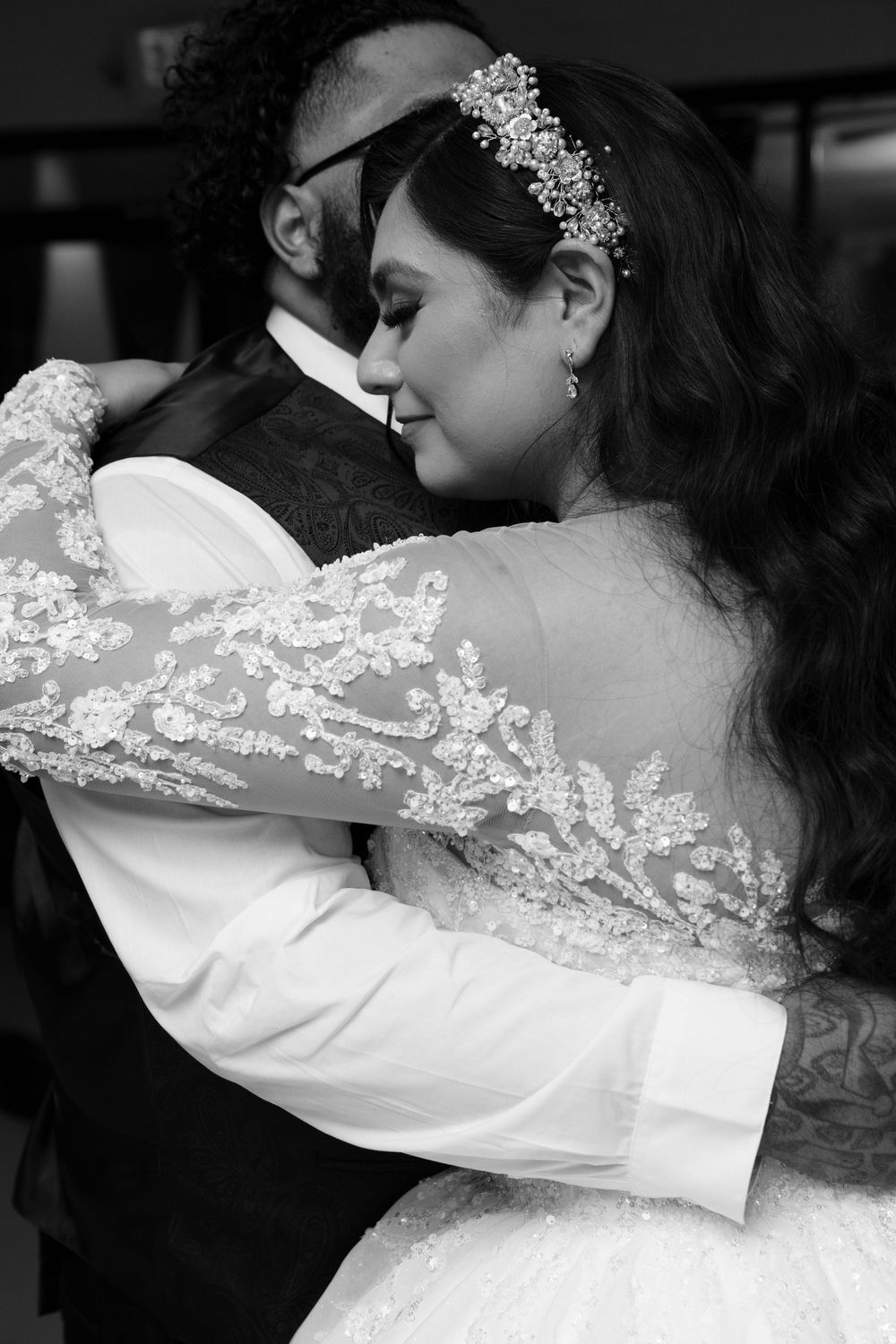 Black and white photo of a bride in lace gown and groom sharing a tender embrace during their first dance.