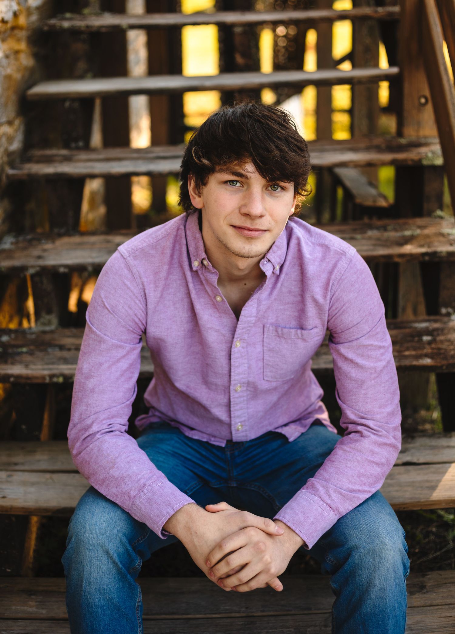 Senior boy dressed in a purple button up and jeans sits on steps at an old mill, by Charlottesville family and newborn photographer.