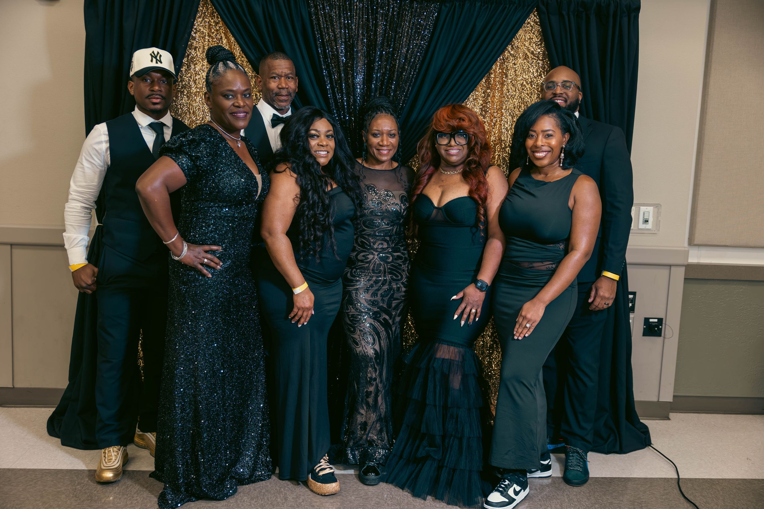 Group of elegantly dressed people posing together in dark formal attire at a special event.