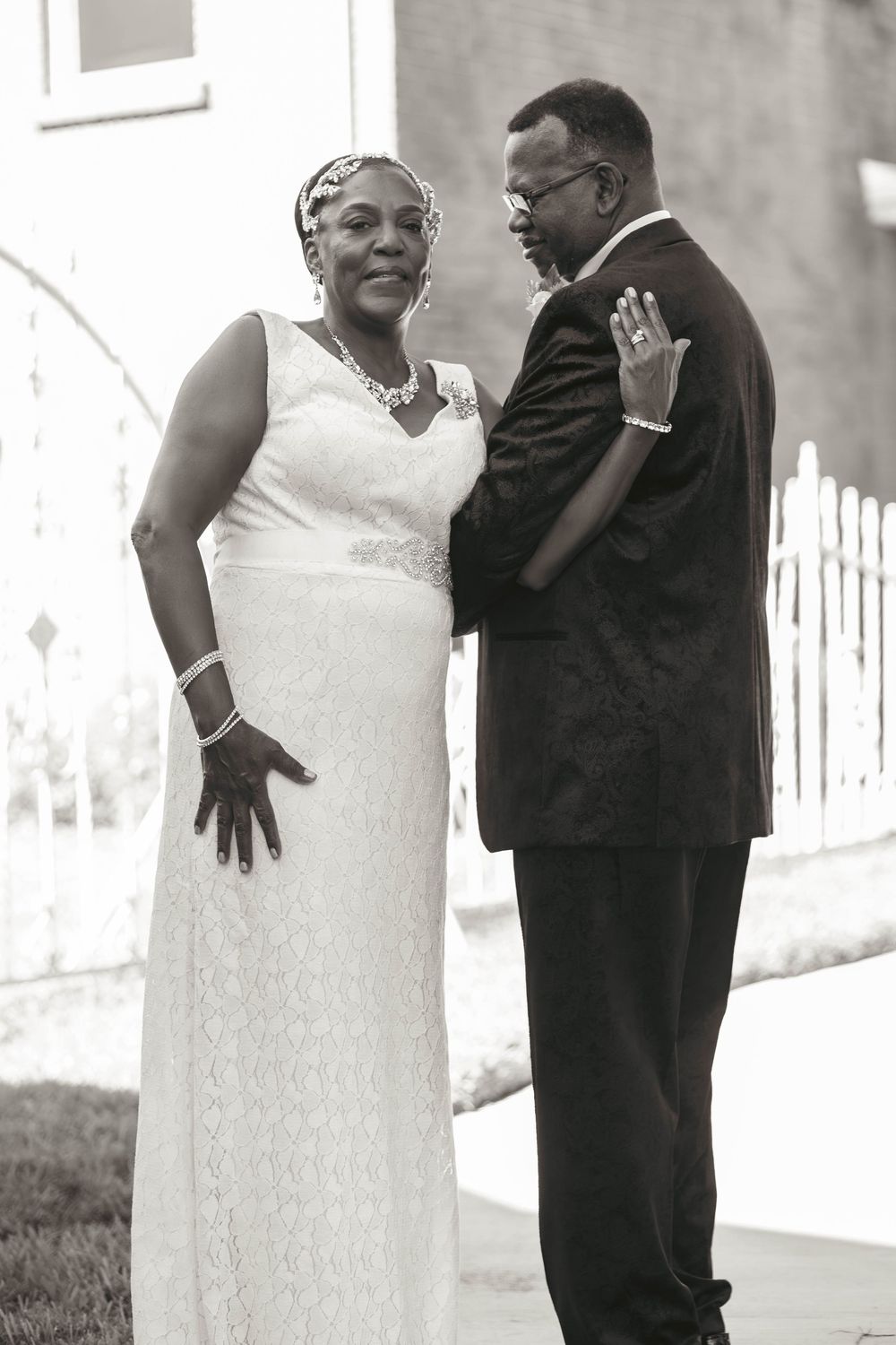 Black and white photo of a couple in wedding attire, bride in white lace gown and groom in dark suit, sharing a tender moment.