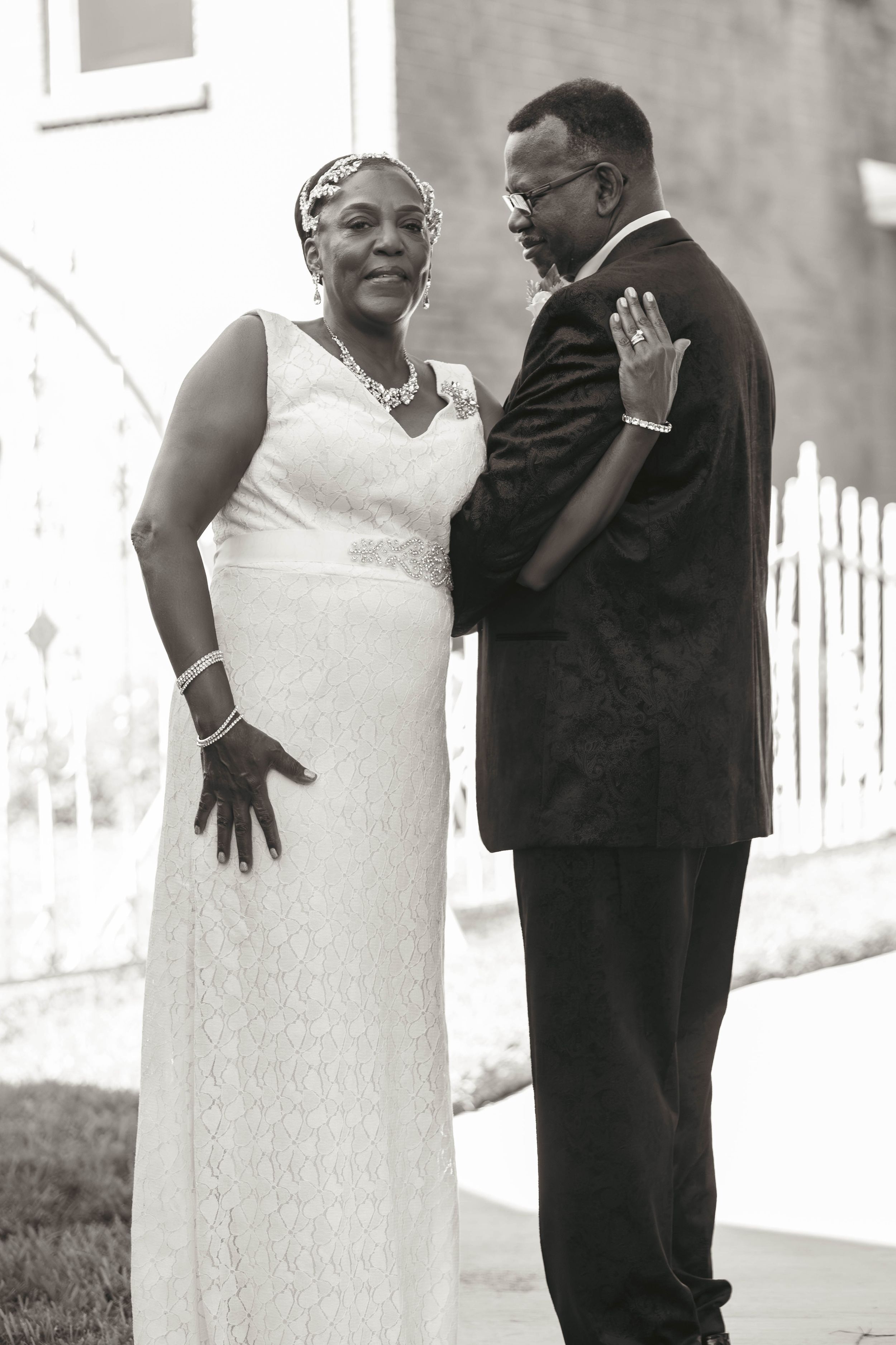Black and white photo of a couple in wedding attire, bride in white lace gown and groom in dark suit, sharing a tender moment.