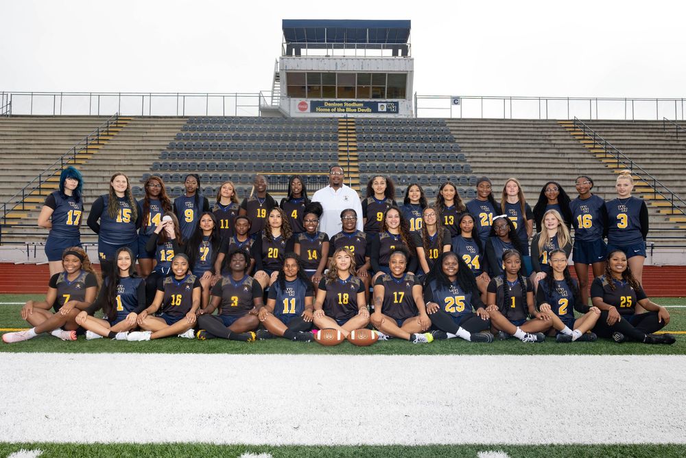 Girls soccer team poses in navy uniforms on stadium field for official group photo.