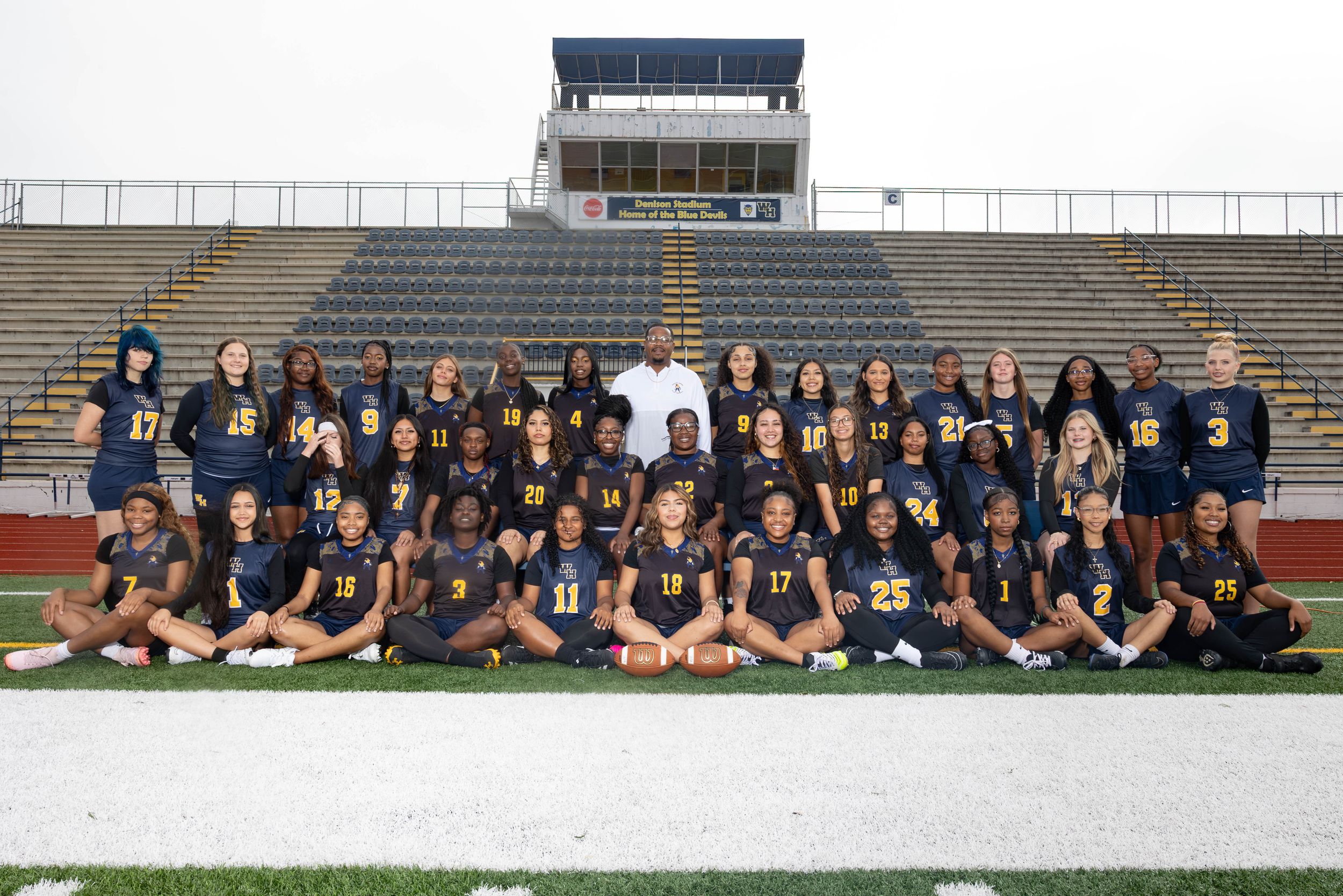 Girls soccer team poses in navy uniforms on stadium field for official group photo.