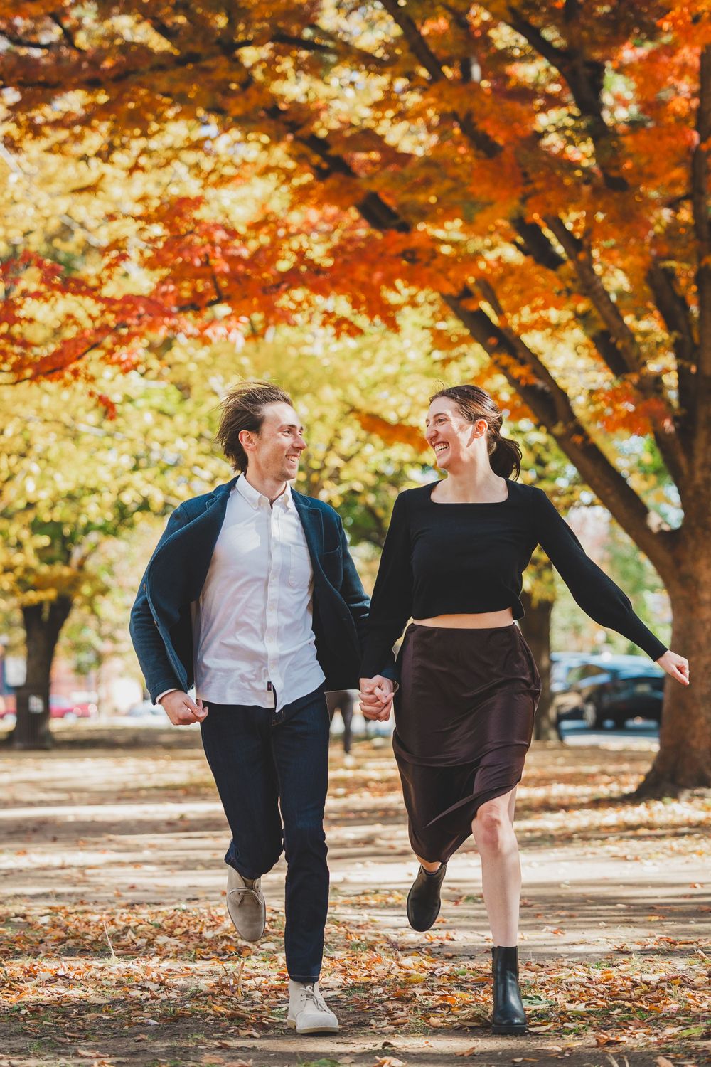 Happy couple holding hands and walking through a colorful autumn park with vibrant red and orange foliage at Lincoln Park DC