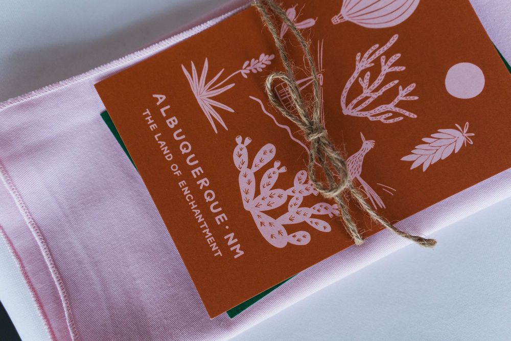 Pink fabric and an orange Albuquerque, NM souvenir card tied with twine, featuring desert plant illustrations.