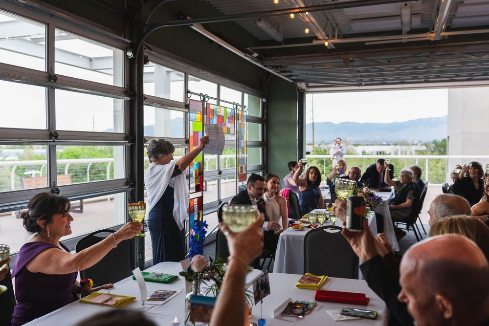 Guests raise glasses in a vibrant dining room with colorful window art and mountain views at a lively event.