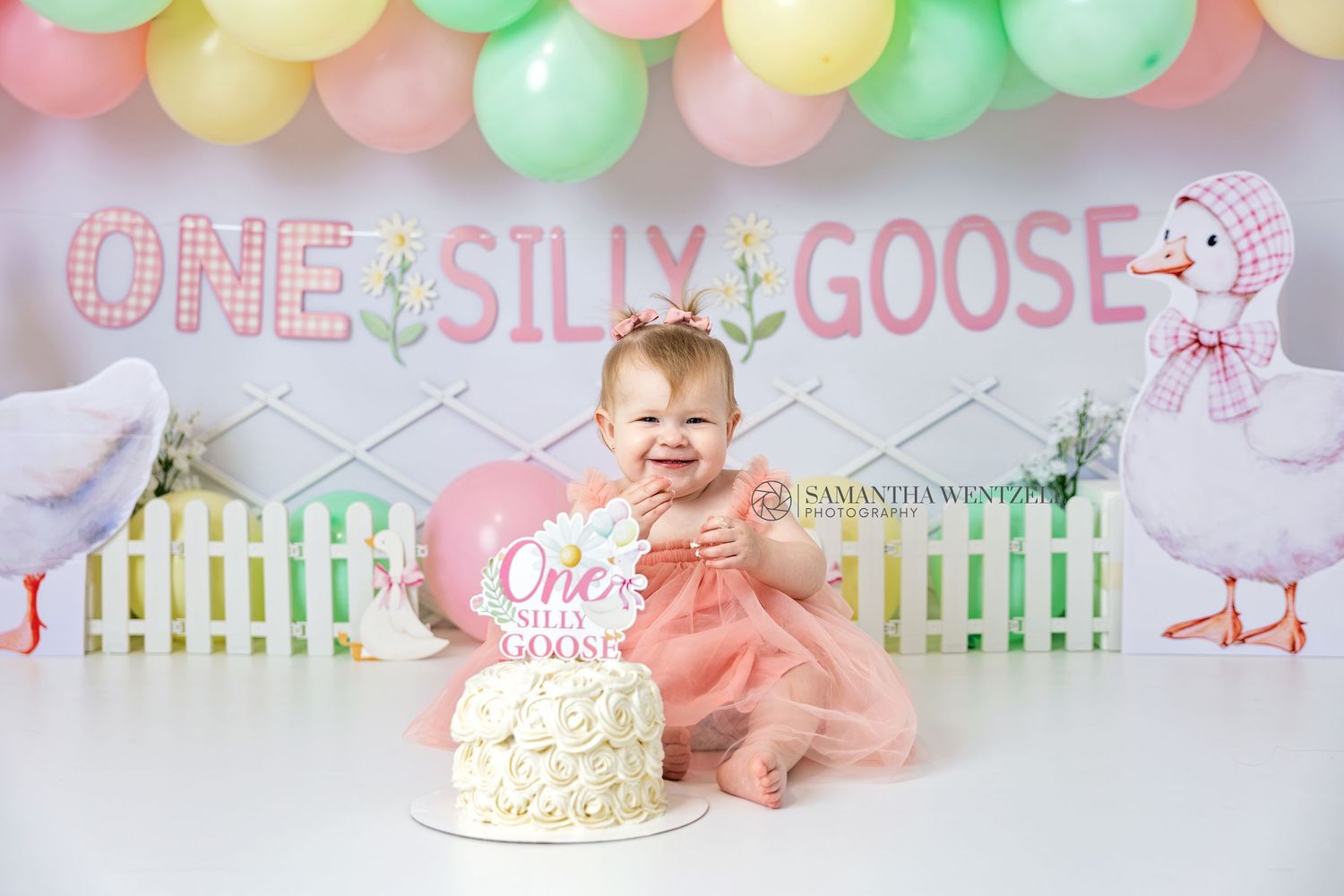 Baby girl in pink tutu smashes first birthday cake at One Silly Goose themed party with balloon decorations.