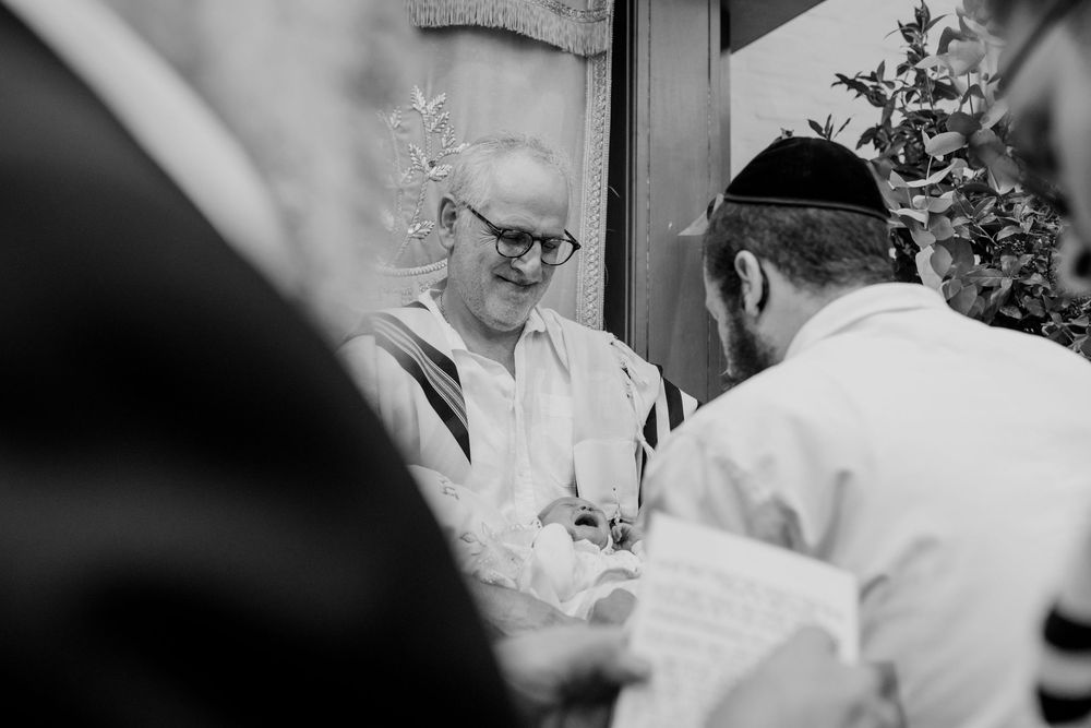 Black and white photo of smiling man in kippah at Jewish ceremony with guests.