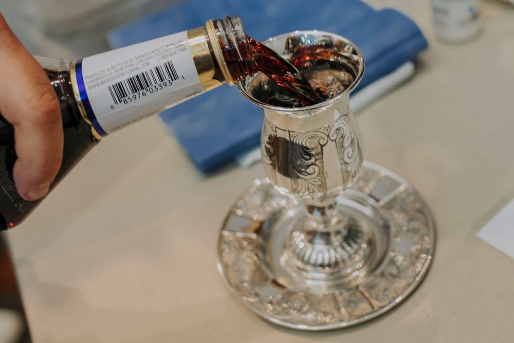Red wine being poured into an ornate silver Kiddush cup on a decorative silver plate for Jewish Shabbat.