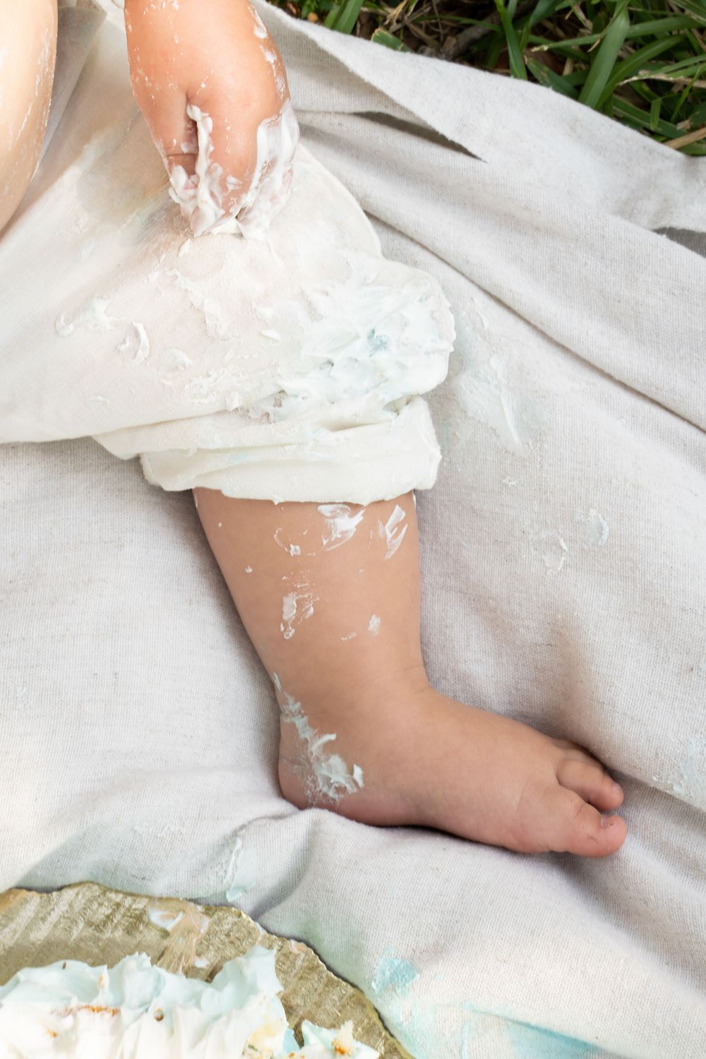 Baby's foot and leg covered in white cake frosting on a white blanket during a first birthday cake smash.