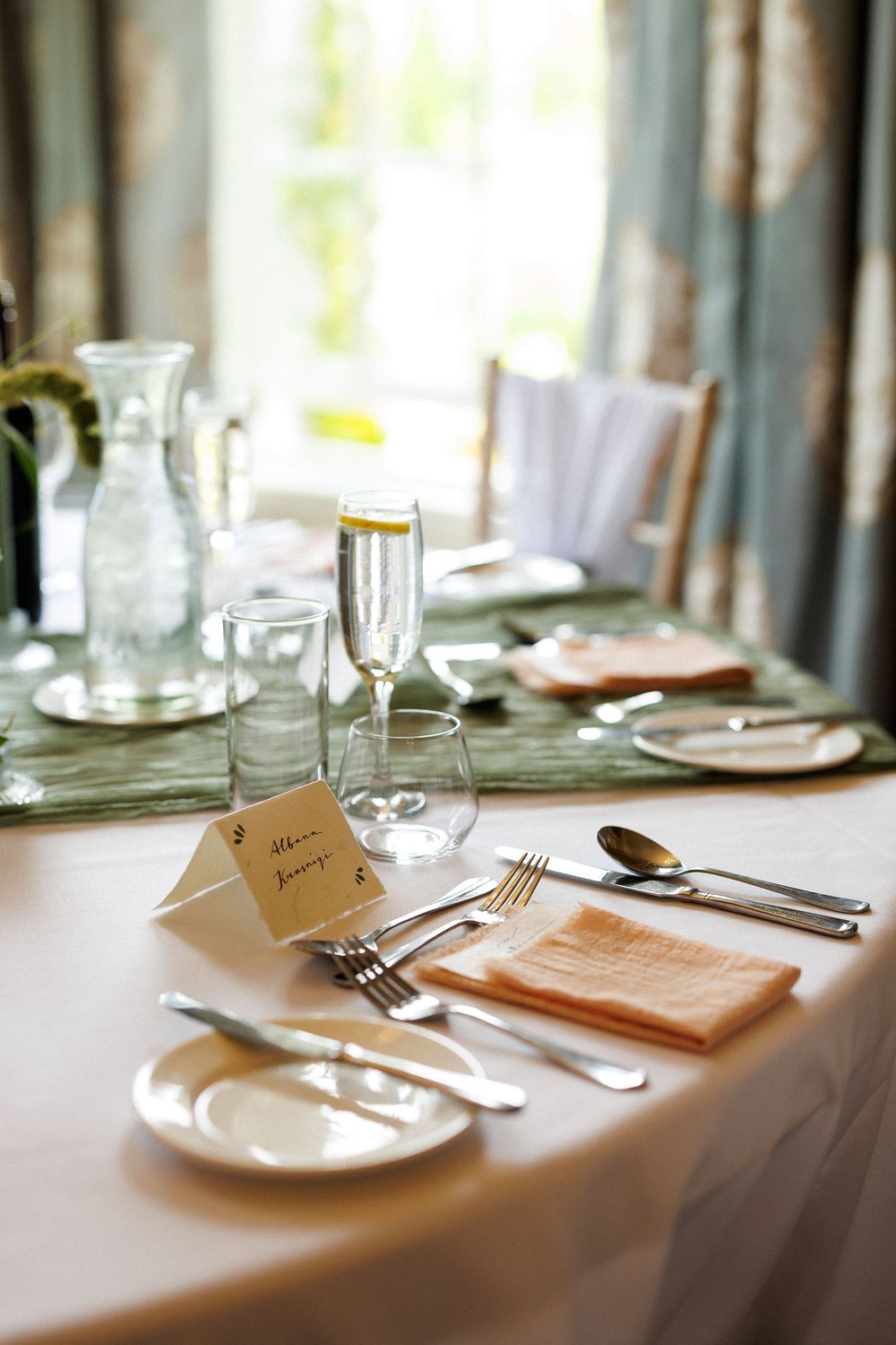 Elegant wedding table setting with champagne flutes, silverware, peach napkins, and place cards on a white tablecloth.