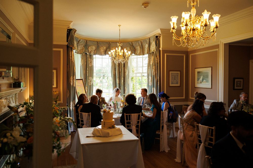 Elegant wedding reception in a grand dining room with chandelier lighting and guests seated at decorated tables.