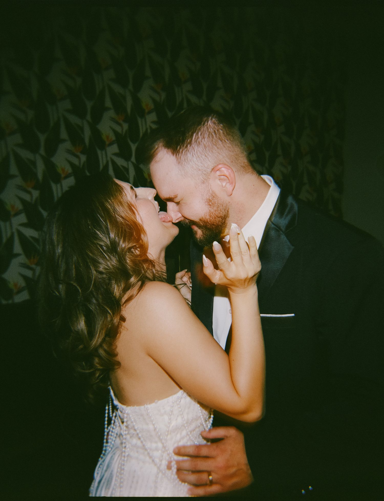 A couple in wedding attire shares a romantic almost-kiss moment, the bride in a white gown and groom in a dark suit.