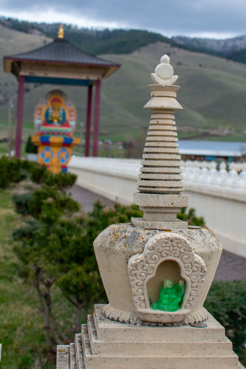 White stone Buddhist stupa with small green Buddha figurine at a mountain temple site.