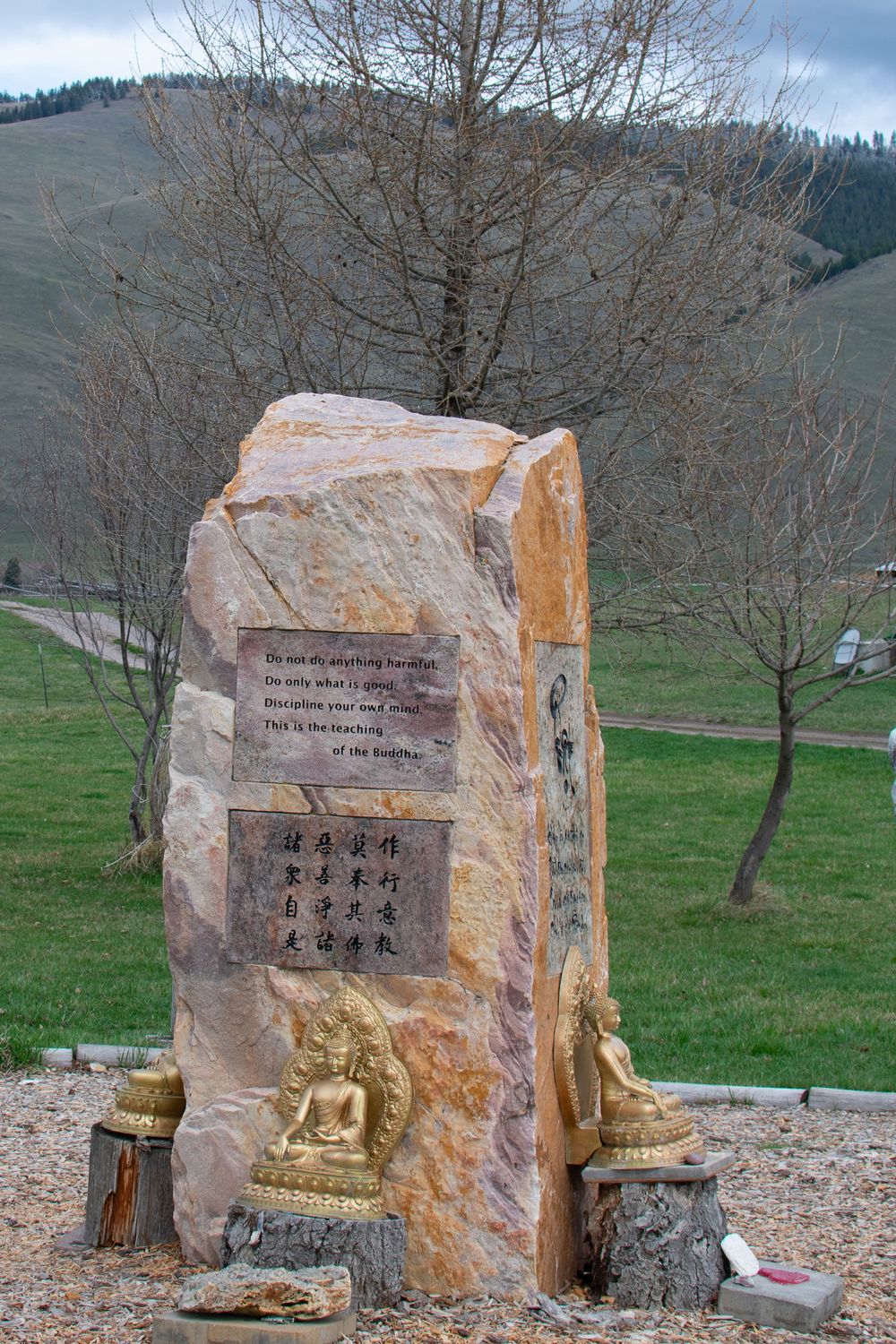 Buddhist stone monument with Chinese inscriptions and golden Buddha statues in mountain landscape.