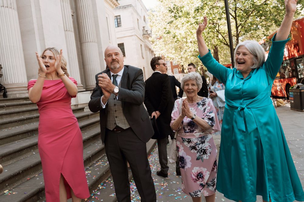 Joyful group of people celebrating outdoors, clapping and cheering, dressed in formal attire with confetti falling.