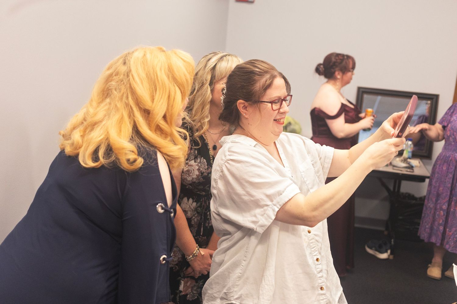 Women gathered indoors, one showing content on a smartphone screen to another in a casual office setting.