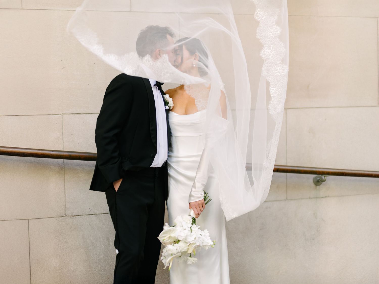 Bride's veil lifting in the wind as she and the groom stand close outdoors.
