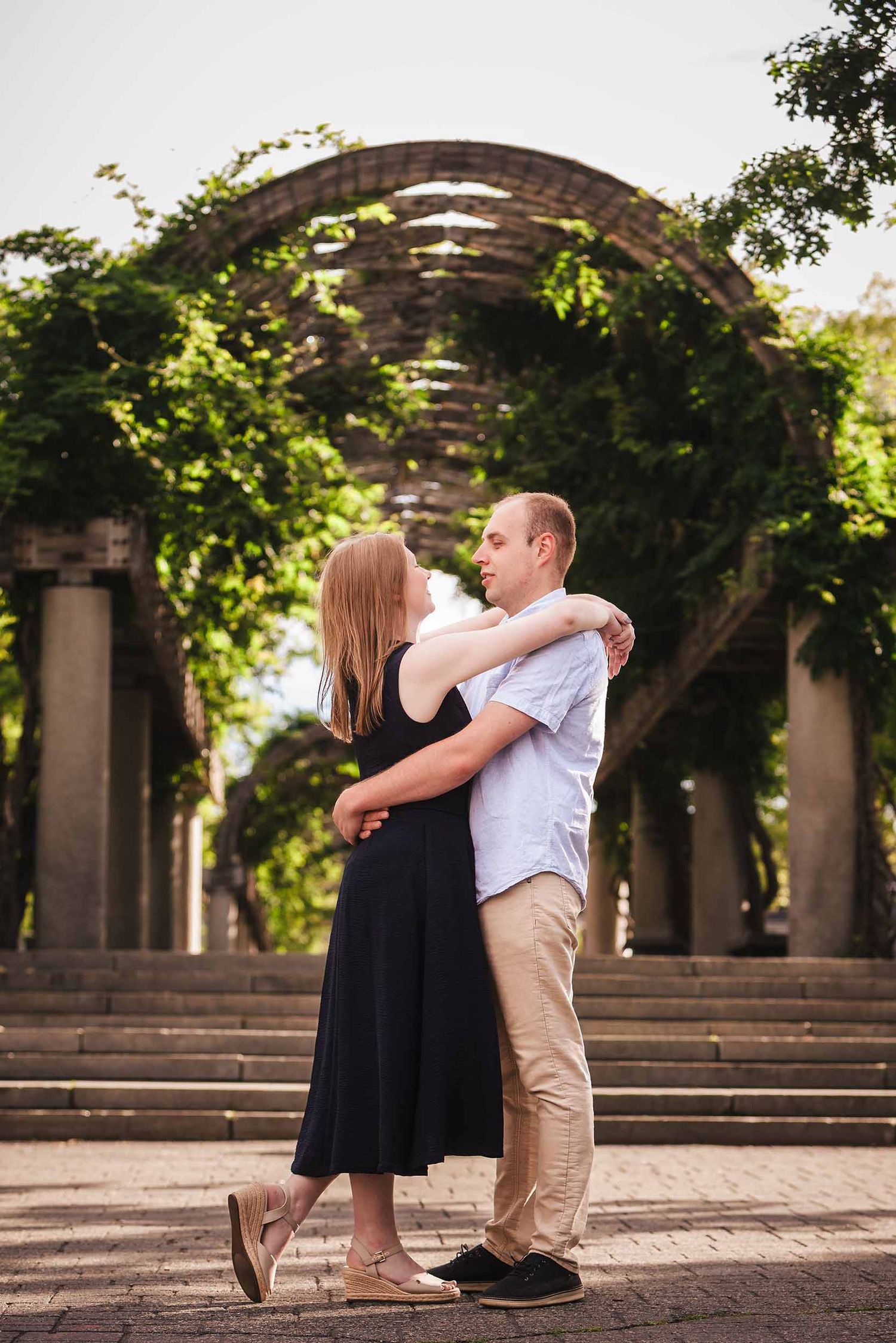 Engaged couple embracing under the wooden pergola arch at Christopher Columbus Park in Boston