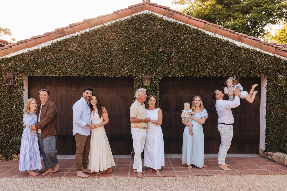 Multi generational family portrait of multiple generations posing in front of ivy-covered garage in warm natural light vacationing together