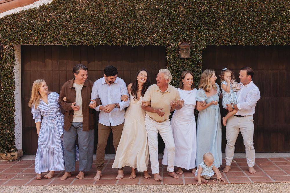Multi-generational family portrait outdoors, smiling group of eight adults and children in coordinated blue and white outfits.