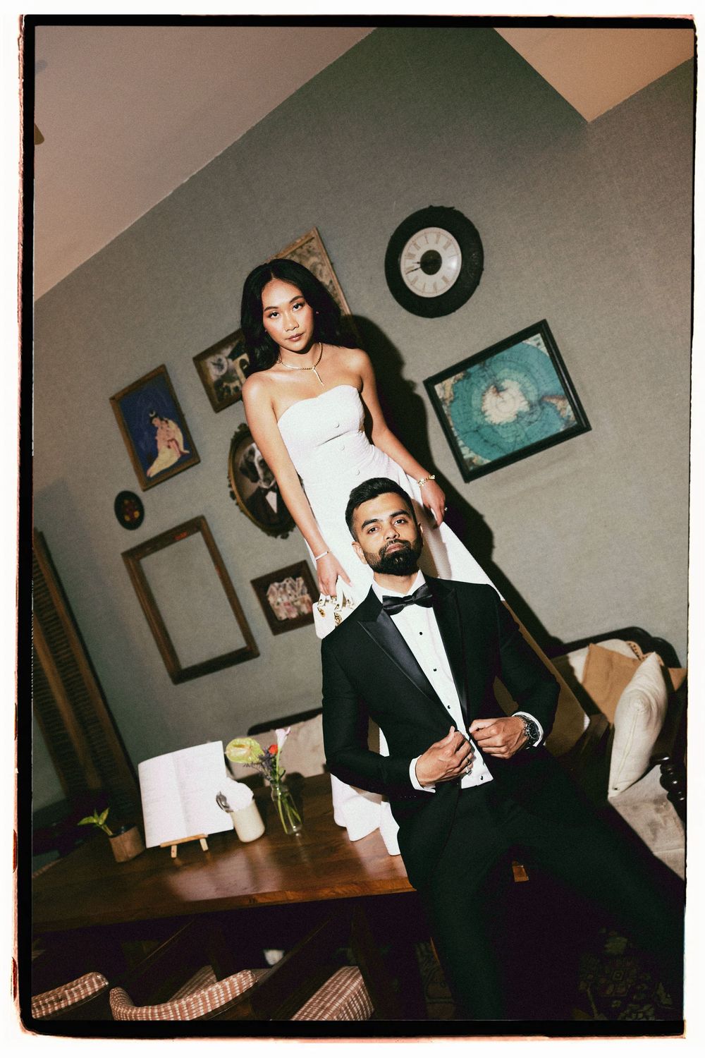Elegant couple in formal wear, woman in white gown and man in black tuxedo, posing in a stylish room.
