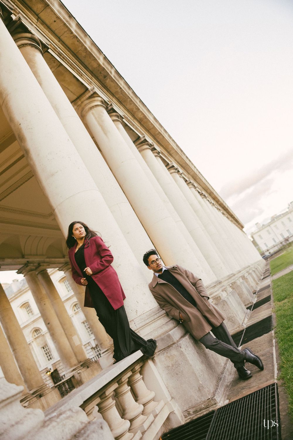 Couple posing by grand white columns of a classical building, woman in red coat and man in tan coat.