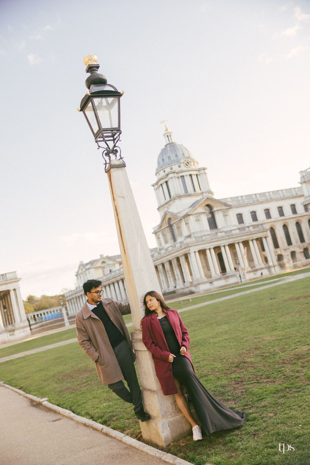 Couple posing by a lamp post at the Old Royal Naval College in Greenwich, London, on a clear day.