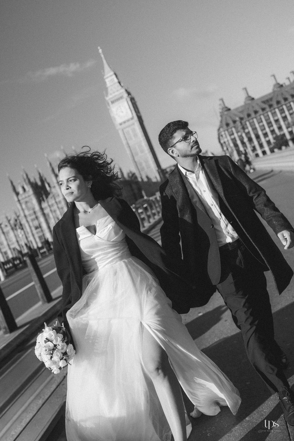 Black and white wedding photo of a couple walking near Big Ben and Houses of Parliament in London, bride holding bouquet.
