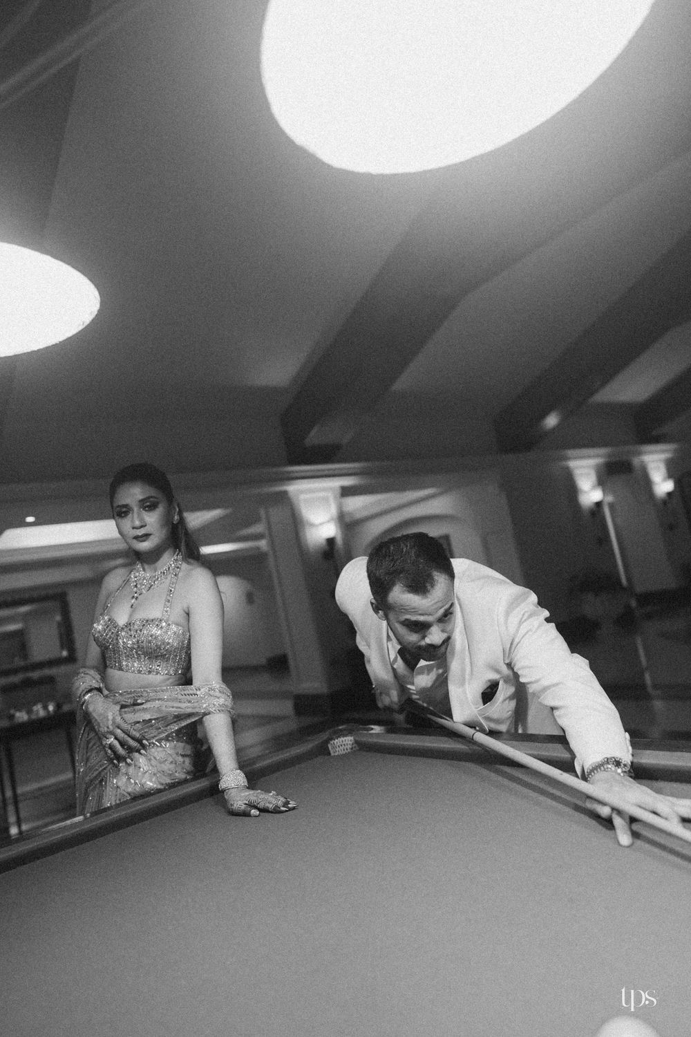 Black and white photo of a couple at a billiard table, man leaning to take a shot while woman watches elegantly.
